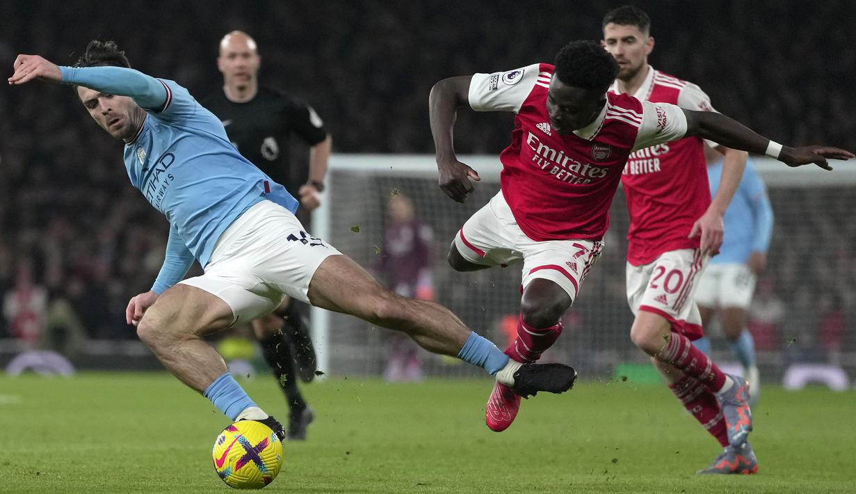 Pemain Manchester City, Jack Grealish (kiri) berebut bola dengan pemain Arsenal, Bukayo Saka pada laga pekan ke-23 Liga Inggris 2022/2023 yang berlangsung di Emirates Stadium, London, Kamis (16/02/2023) WIB. The Cityzens berhasil menang dengan skor 3-1. (AP Photo/Kin Cheung)
