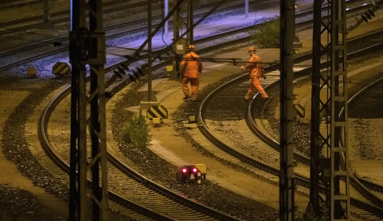 Dua karyawan kereta api berjalan di belakang sinyal merah melintasi rel di Stasiun Barang Maschen, Maschen, Jerman, Selasa (10/8/2021). Serikat masinis kereta api Jerman mogok kerja selama tiga hari untuk menuntut kenaikan upah. (Jonas Walzberg/dpa via AP)