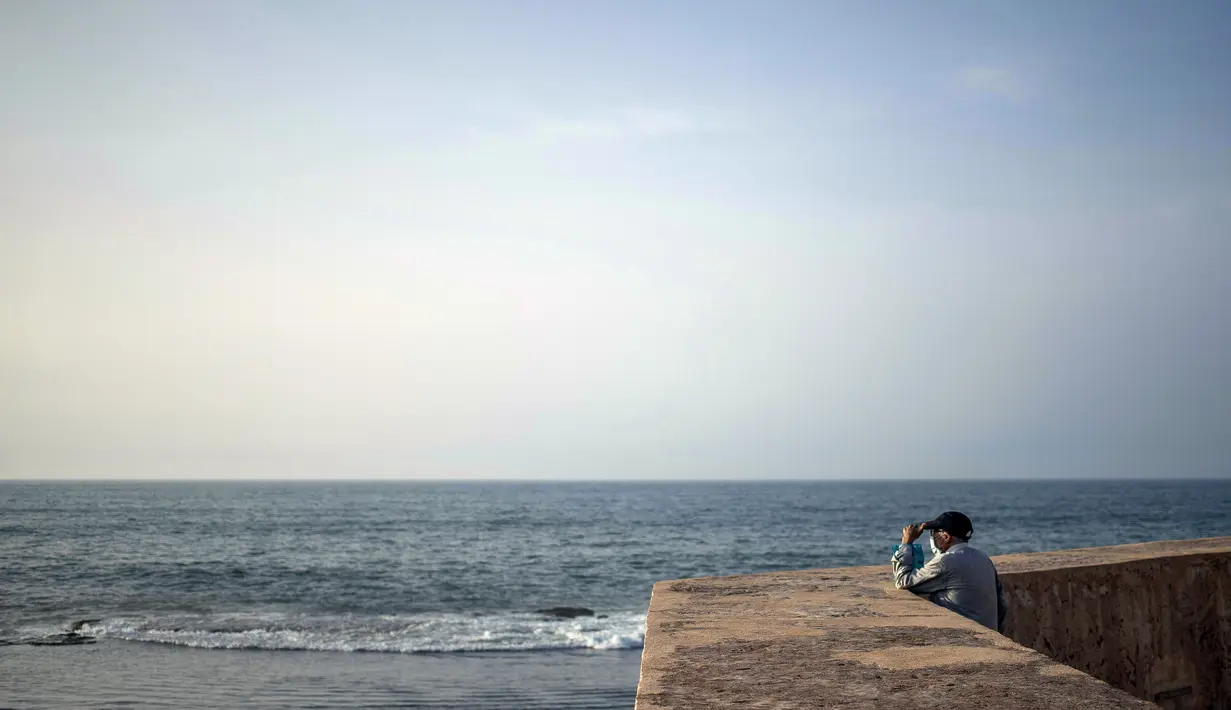 Seorang pria yang memakai masker wajah untuk mencegah penyebaran virus corona memandang ke Samudra Atlantik sebelum matahari terbenam, di Rabat, Maroko, Selasa (22/9/2020). (AP Photo / Mosa'ab Elshamy)