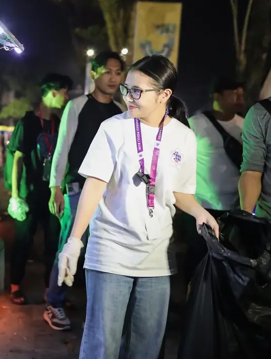 <p>Mengenenakan celana jean, kaos putih, dan rambut di ikat, membawa kantong plastik hitam besar dan memungut sampah yang berserakan. [Instagram/prillylatuconsina96]</p>