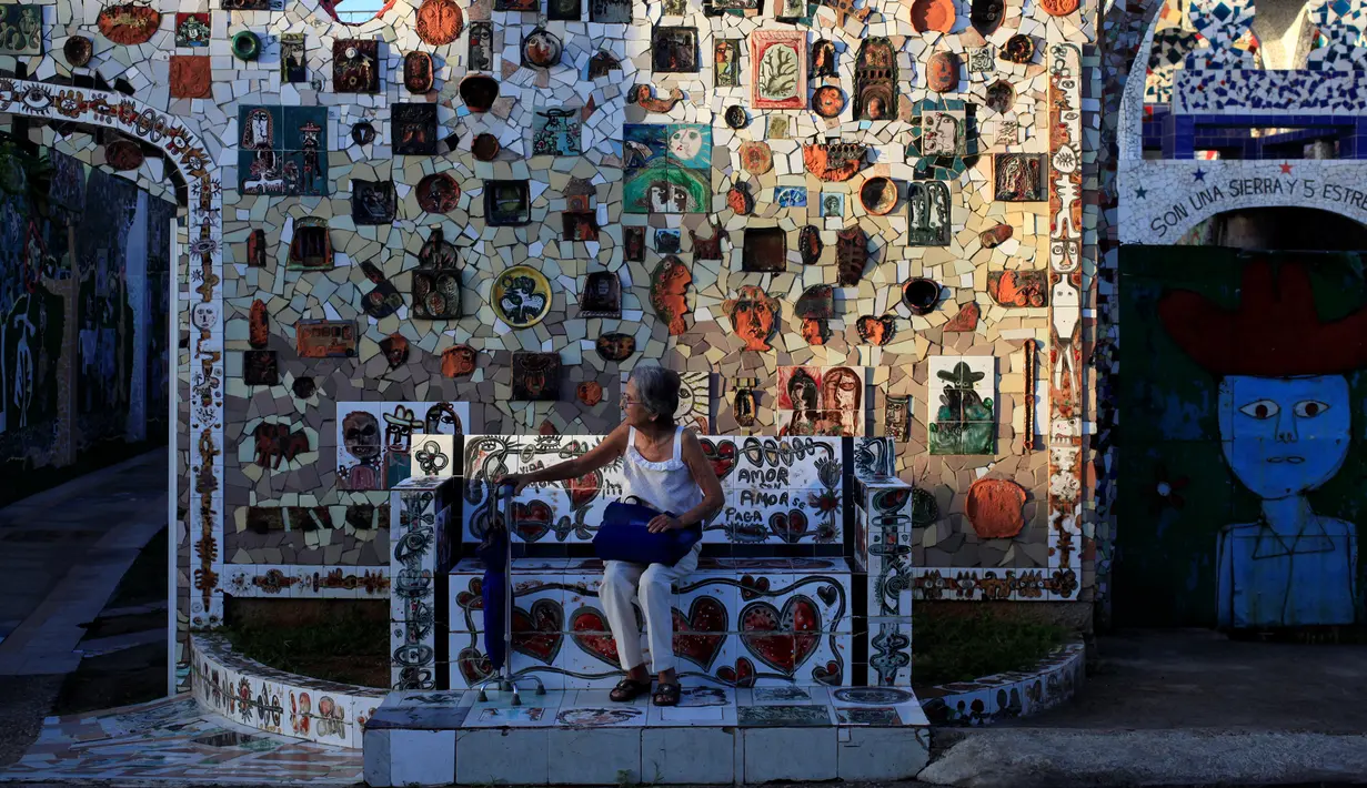 Seorang wanita duduk didepan dinding yang dihiasi dengan mosaik di desa Jaimanitas, Havana, Kuba, (14/7). Fuster juga menghiasi desanya dengan lukisan Picasso. (REUTERS / Enrique de la Osa)