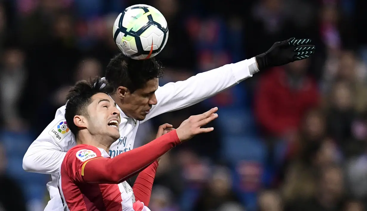 Bek Real Madrid, Raphael Varane, duel udara dengan bek Girona, Juanpe Ramirez, pada laga La Liga di Stadion Santiago Bernabeu, Senin (19/3/2018). Real Madrid menang 6-3 atas Girona. (AFP/Javier Soriano)
