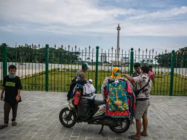 Pedagang kaos cendera mata keliling mencoba peruntungan dari para pengunjung yang ingin menyaksikan Tugu Monas Jakarta dari balik pagar, Sabtu (2/1/2021). (Liputan6.com/Faizal Fanani)