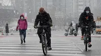 Orang-orang mengendarai sepeda mereka di salju saat mereka menyeberang jalan pada hari bersalju di Beijing pada 20 Januari 2022. Ibu Kota China diselimuti salju pada Kamis, saat hitungan mundur menuju dua minggu Olimpiade Musim Dingin Beijing 2022 dimulai. (Noel Celis / AFP)