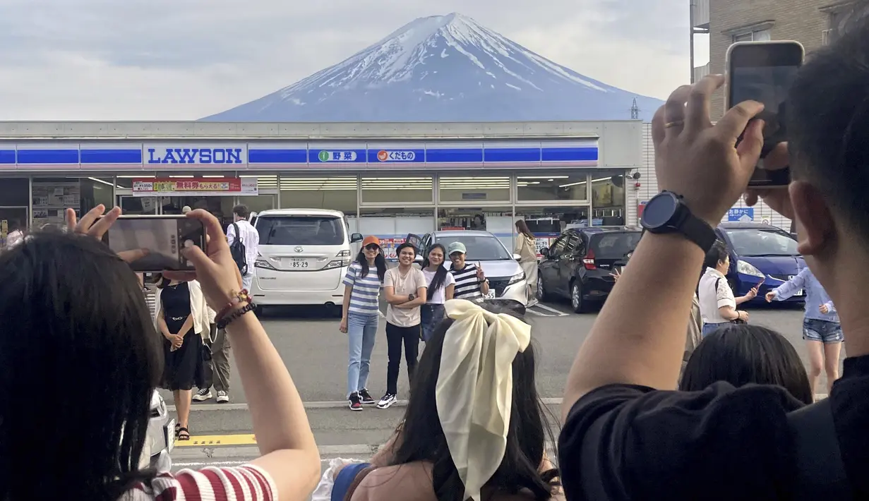 Para pengunjung mengambil foto di depan toko serba ada di kota Fujikawaguchiko, prefektur Yamanashi, Jepang, dengan latar belakang Gunung Fuji pada tanggal 28 April 2024. (Kyodo News via AP)