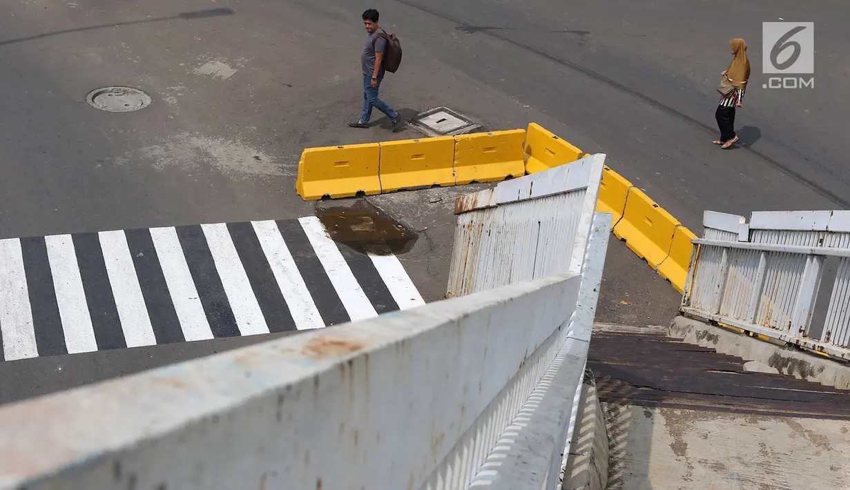 Pejalan kaki melintas di dekat tangga JPO yang berada di tengah jalan Dewi Sartika, Jakarta, Rabu (9/1). Adanya proyek pelebaran jalan menyebabkan posisi trotoar bergeser sehingga tangga JPO menjadi di tengah jalan. (Liputan6.com/Immanuel Antonius)