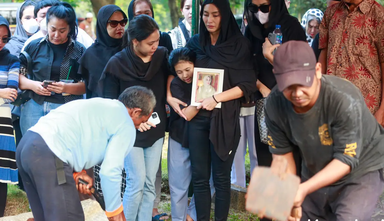 Sambil memegang bingkai foto sang ibunda, tatapan terus ke arah tempat sang ibu dimakamkan. Tampak beberapa petugas menguruk tanah. [Foto: Muhammad Akrom Sukarya/KapanLagi.com]