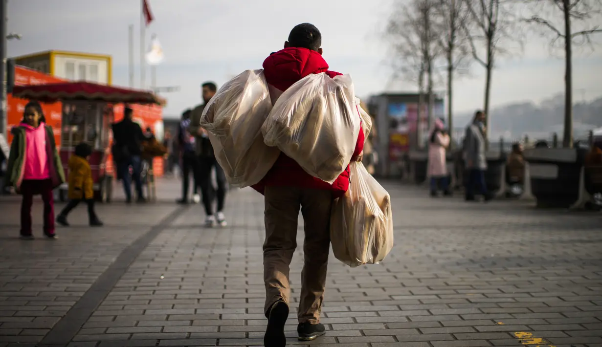 Seorang pria membawa tas penuh roti di kawasan pejalan kaki Karakoy di Istanbul, Turki (9/1/2022). Meskipun ada lonjakan, negara tersebut belum mempertimbangkan untuk memberlakukan pembatasan baru. (AP/Francisco Seco)