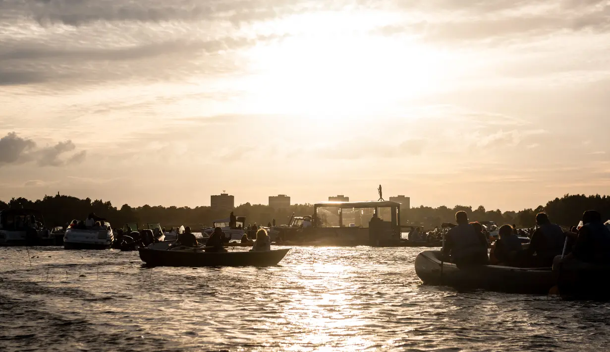 Para penonton menikmati konser musik Laivā dari atas perahu di Danau Juglas, Riga, Latvia, 14 Agustus 2021. Warga Latvia bisa menikmati konser musik dari atas kayak, sampan, dan kapal motor bahkan ketika mereka belum divaksin COVID-19. (Gints Ivuskans/AFP)