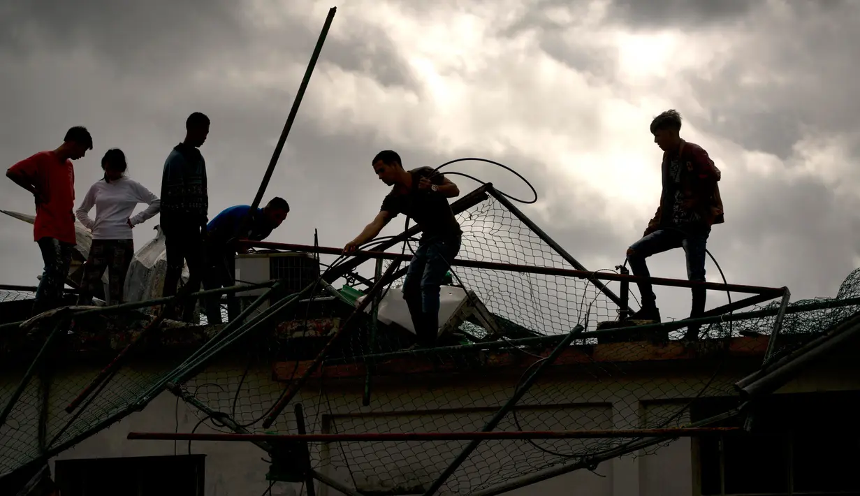 Sejumlah warga membersihkan puing-puing di sebuah bangunan setelah badai tornado menghantam Regla, Kuba (28/1). Hantaman tornado juga merobohkan tiang-tiang listrik di daerah tersebut. (AP Photo/Ramon Espinosa)