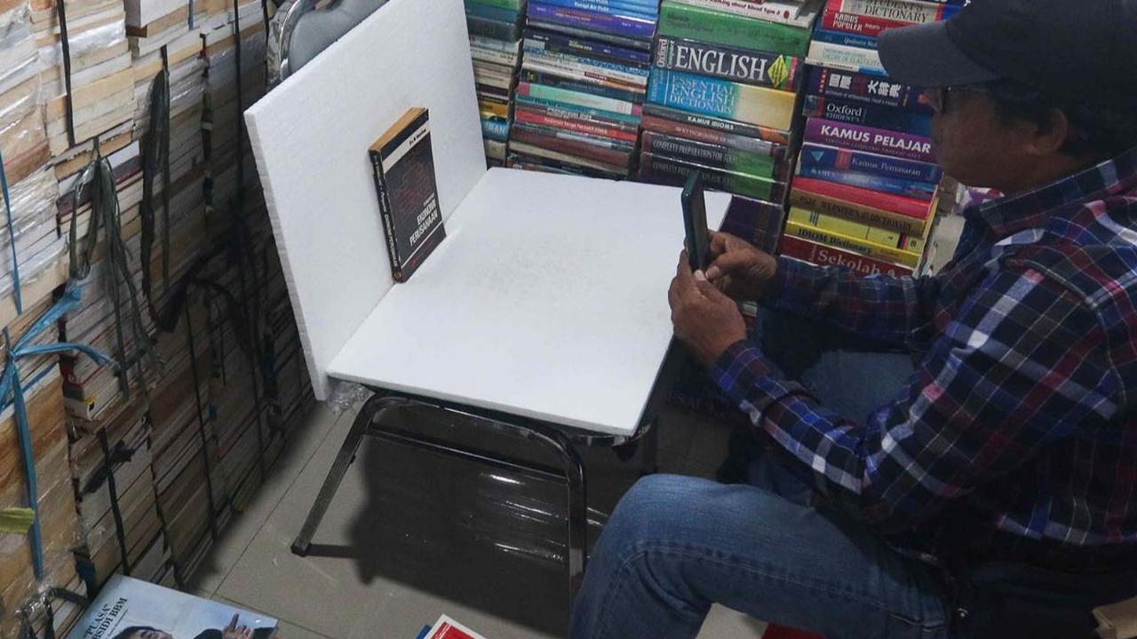 Pedagang memotret buku yang hendak dipasarkan secara online di kiosnya di Sentra Buku Pasar Kenari, Jakarta, Selasa (30/1/2024). Kondisi Pasar Kenari yang sepi pengunjung membuat pedagang buku mengalami penurunan omset. Foto: Liputan6.com/Herman Zakharia<