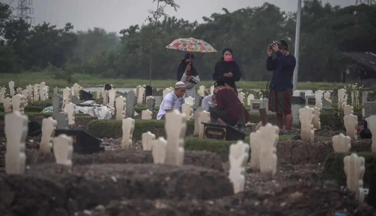 Keluarga berkumpul di dekat kuburan korban virus Corona Covid-19 di tengah hujan lebat di pemakaman Keputih, Surabaya (7/1/2020). Data Surabaya Lawan Covid-19 per 5 Januari 2021 menyebutkan, ada kenaikan 0.27 persen sehingga total kasus positif di Surabaya menjadi 18.399 kasus. (AFP/Juni Kriswanto)