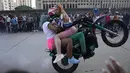 Pengendara sepeda motor, dengan dua penumpang wanita, melakukan wheelie di sepeda motornya selama pameran di lingkungan El Valle Caracas, Venezuela, Sabtu (31/7/2021). (AP Photo/Ariana Cubillos)