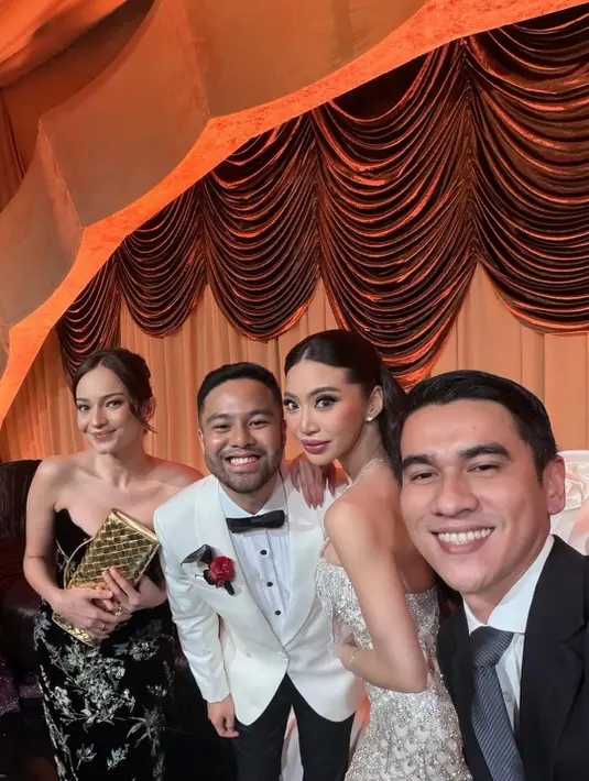 Enzy tampil chic dalam gaun hitam dengan detail floral embroidery bernuansa sheer di bagian rok, menciptakan siluet feminin namun tetap formal. Ia memadukannya dengan clutch emas yang menjadi statement.  Molen tampil kontras dengan tuxedo putih–hitam, lengkap dengan bow tie dan boutonniere merah, memberi sentuhan klasik ala pesta malam yang elegan. [@enzystoria].