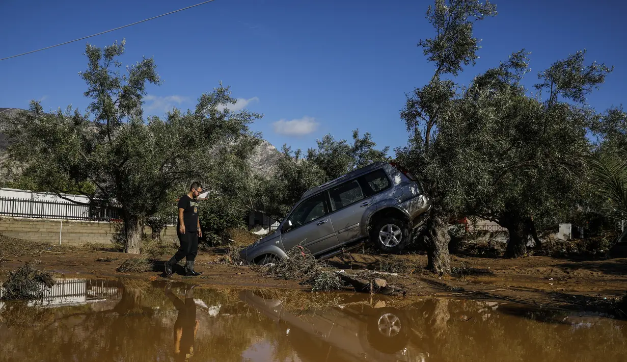 Seorang pria berjalan melewati sebuah mobil yang terbawa air banjir setelah badai di desa Kineta, Athena (25/11/2019). Ratusan rumah terendam banjir setelah badai semalam menerjang daerah barat Athena. (AP Photo/Petros Giannakouris)
