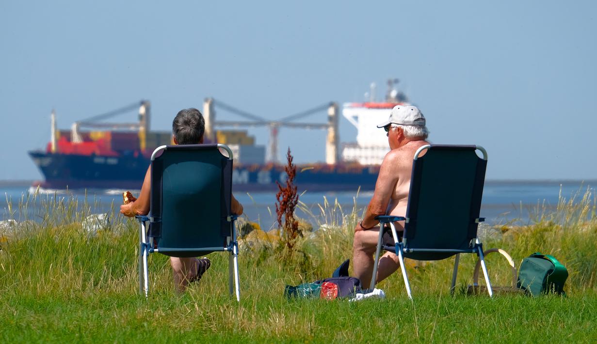 Warga berjemur ketika kapal kargo menuju Laut Utara saat suhu mencapai 34 derajat Celcius di dekat pantai Laut Utara di Wremen, Jerman barat (24/7/2019). (AFP Photo/Patrik Stollarz)