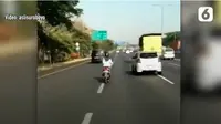 Seorang wanita berhijab dengan skuter matik melintasi jalan tol