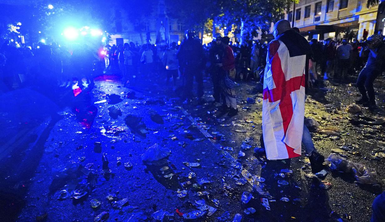 Seorang suporter menenteng bendera nasional Inggris berjalan diantara sampah yang berserakan di Kota London paska final Euro 2020 antara Timnas Inggris melawan Italia. (Foto:AP/Victoria Jones)