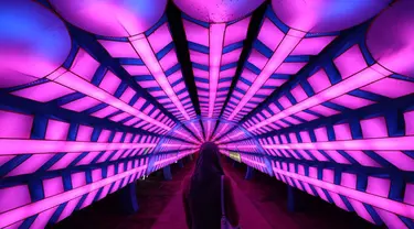 Seorang wanita berjalan melewati instalasi lampu di Dubai Garden Glow, Dubai, Uni Emirat Arab, 1 November 2021. Instalasi tersebut dibuat dari lebih satu juta bohlam penghemat energi dan kain bercahaya daur ulang karya seniman seluruh dunia. (GIUSEPPE CACACE/AFP)