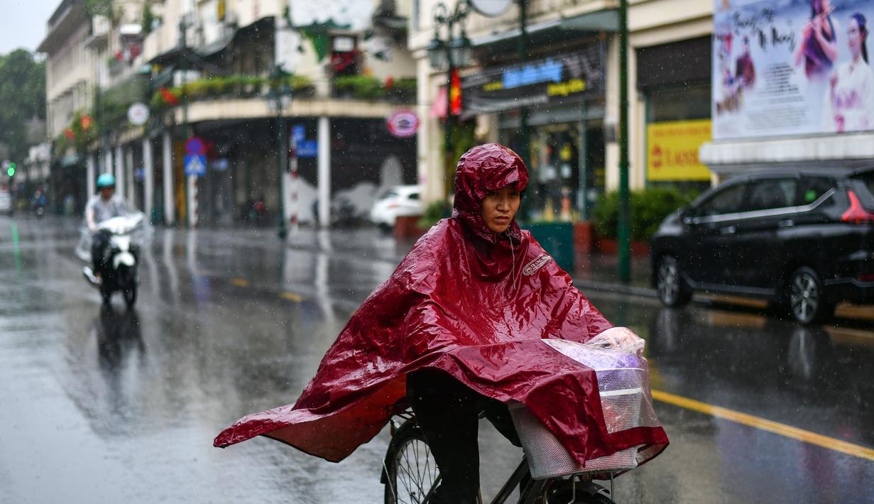 Pejalan kaki yang mengenakan jas hujan mengendarai sepeda saat hujan deras di Hanoi (14/10/2020). Badai tropis Nangka menghantam Vietnam tengah-utara yang mengakibatkan bencana alam, terutama hujan lebat dan banjir, telah menyebabkan 28 orang tewas dan 12 lainnya hilang. (AFP Photo/Manan Vatsyayana)