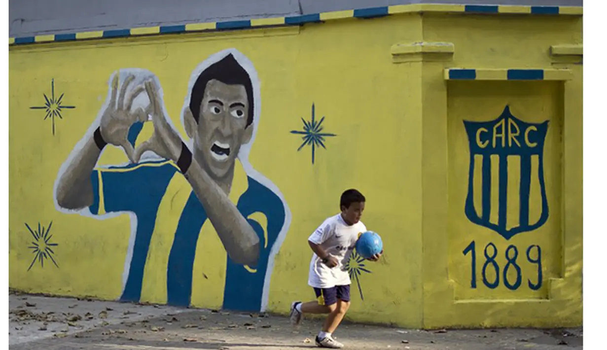 Seorang anak melewati mural bergambar Angel Di Maria menggunakan kostum Central Rosario di Santa Fe, Argentina, Minggu (5/4/2015). Central Rosario merupakan klub pertama Di Maria saat memulai karier profesional. (AFP Photo/Hector Rio)