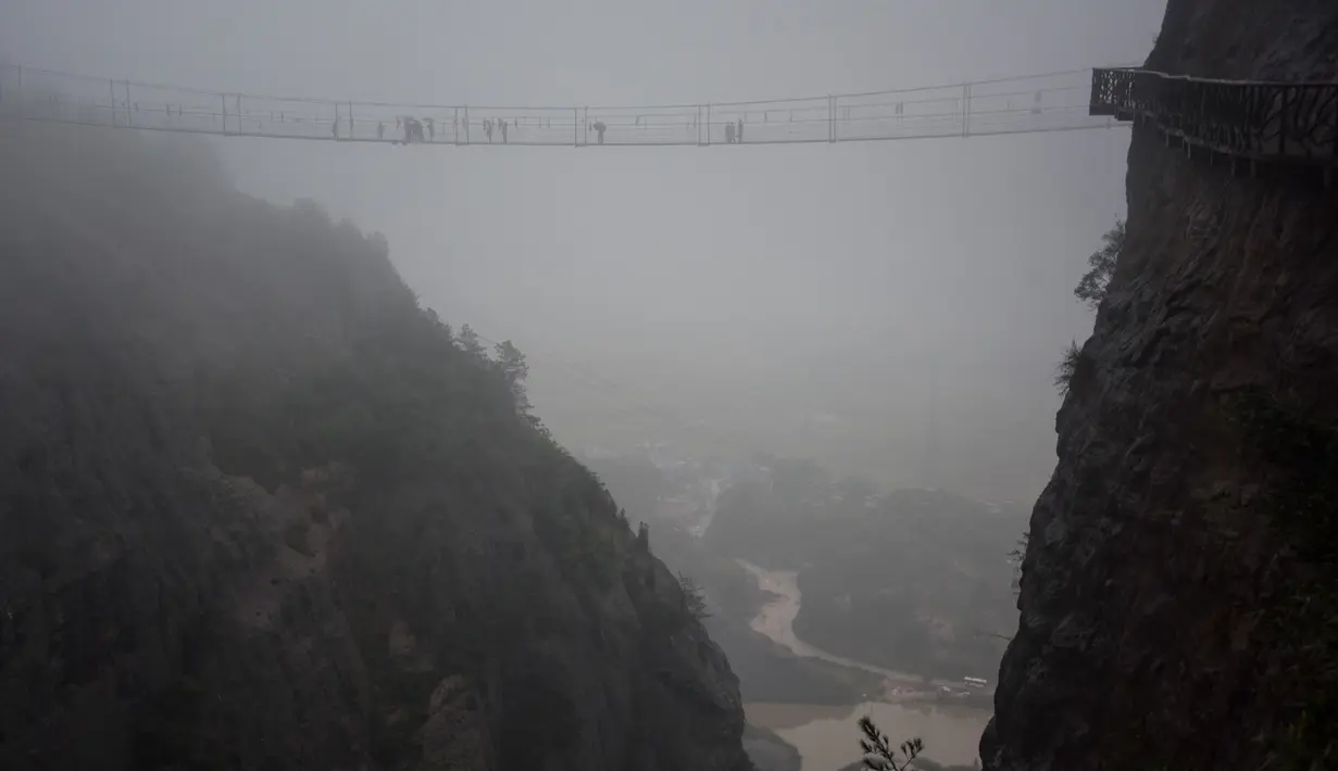 Wisatawan melewati jembatan gantung yang terbuat dari kaca di pegunungan Shinuizhai, Provinsi Hunan, Tiongkok, 6 Oktober 2015. Jembatan dengan panjang 300 m dan tinggi 180 m ini kembali dibuka setelah direnovasi untuk objek wisata. (AFP/Johannes Eisele)