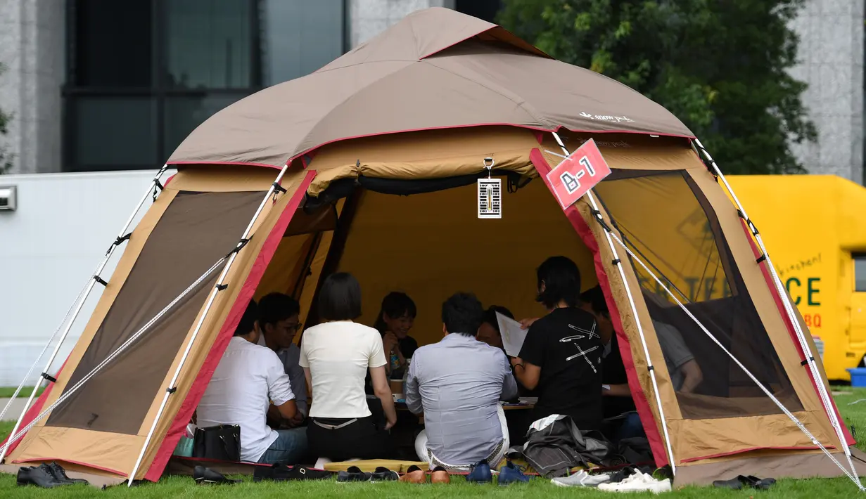 Foto 11 September 2018, karyawan perusahaan bekerja di dalam tenda kemah di halaman luar gedung kantor di Tokyo. Beberapa kantor di Jepang membebaskan pegawainya untuk bekerja di mana saja, mulai dari tenda hingga tempat karaoke. (Toshifumi KITAMURA/AFP)