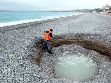Seorang pria turun melihat kawah misterius berisi air payau yang muncul di Pantai Lido, Nice, Prancis, Kamis (1/2). Lubang selebar 5 meter dan sedalam 2 meter itu membuat banyak warga sekitar kebingungan. (VALERY HACHE/AFP)