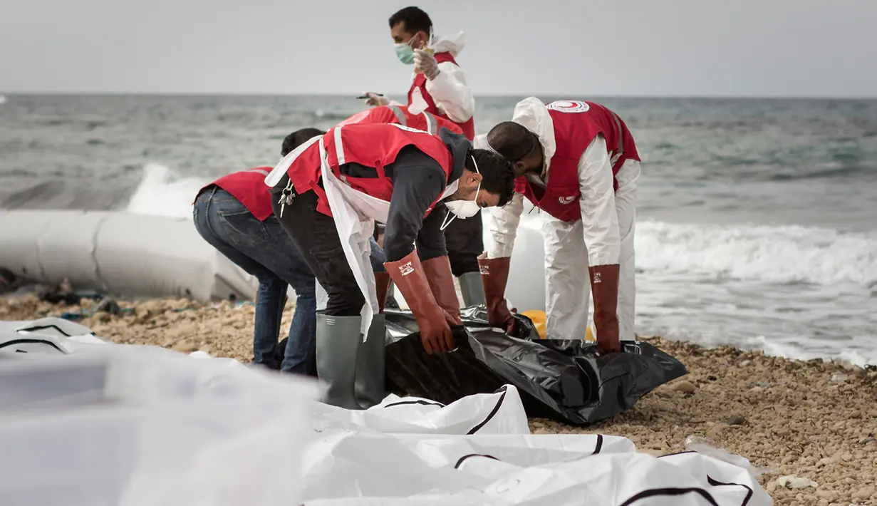 Petugas Bulan Sabit Merah Libya mengumpulkan jenazah para imigran yang ditemukan terdampar di pantai utara Libya, Selasa (21/2). Sedikitnya 74 jenazah imigran tenggelam saat melintasi perairan Mediterania dalam upaya mencapai Eropa. (AMIN ELAMR/AFP)