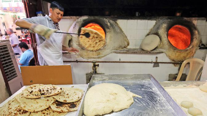 Tukang roti mengangkat roti Iran atau taftoon setelah dipanggang dalam oven tradisional di sebuah toko di Kuwait City, Kuwait, 27 Juni 2019. Beberapa orang Kuwait biasanya menambahkan taftoon dengan wijen, thyme, adas, hingga kurma. (YASSER AL-ZAYYAT/AFP)