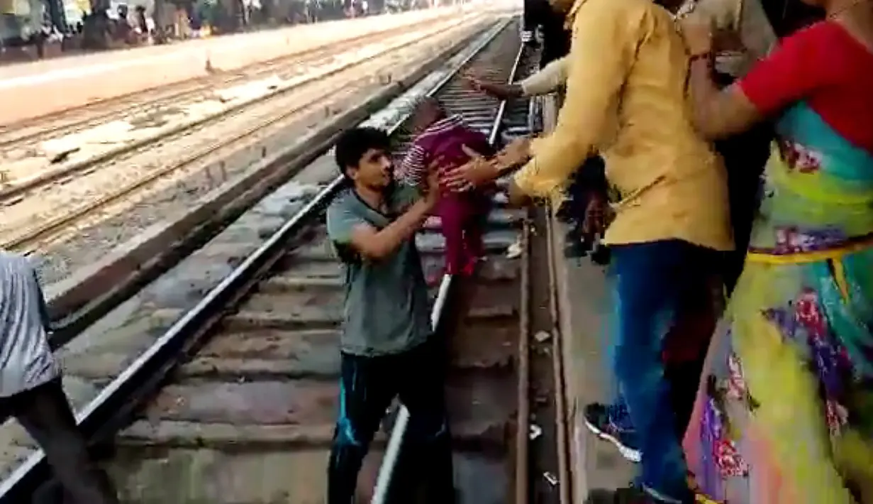 Gambar dari video pada 20 November 2018, seorang pria India menggendong bayi dan memberikan kepada ibunya  setelah terjatuh di samping rel di stasiun kereta api di Mathura, Uttar Pradesh. Bayi satu tahun itu selamat tanpa luka sedikitpun. (NNIS / AFP)