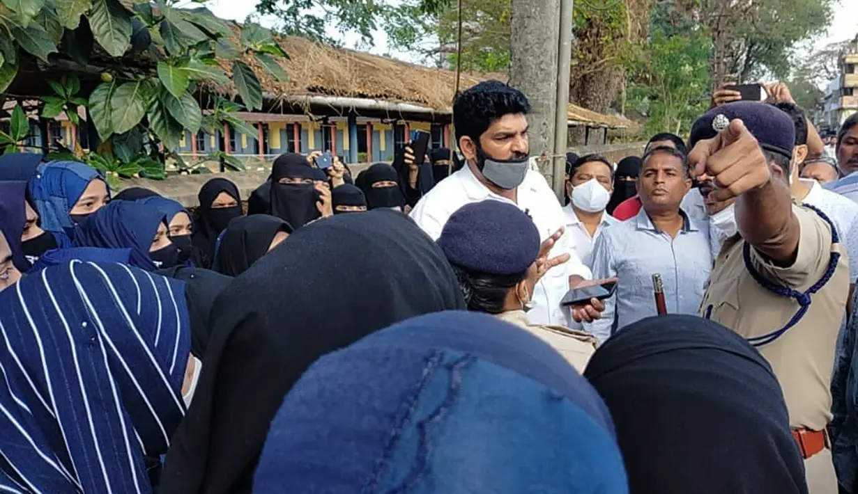Orang tua siswi India yang dilarang masuk ke ruang kelas mereka karena mengenakan jilbab berdebat dengan seorang petugas polisi di luar gedung kampus di Udupi, India, Jumat, 4 Februari 2022. (Bangalore News Photos via AP)