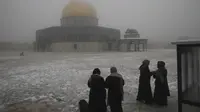 Para wanita berdiri di dekat the Dome of the Rock atau Kubah Batu di kompleks Masjid Al Aqsa pada pagi bersalju di Kota Tua Yerusalem (18/2/2021). Fenomena ini terbilang langka karena baru kembali terjadi pertama kali dalam enam tahun terakhir. (AP Photo/Mahmoud Illean)