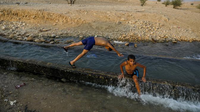 Anak-anak bermain di aliran mata air yang digunakan untuk irigasi untuk mendinginkan tubuh saat suhu udara mencapai 44 derajat Celcius di kota Jericho, Tepi Barat (1/9/2020). (AFP Photo/Ahmad Gharabli)