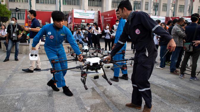 Dua relawan membawa drone untuk menurunkan hujan buatan selama demontrasi di Bangkok, Kamis (31/1). Operasi pengurangan polusi udara dilakukan dengan menggunakan drone untuk menurunkan hujan buatan dengan cara menyemprotkan bahan kimia. (Jewel SAMAD/AFP)