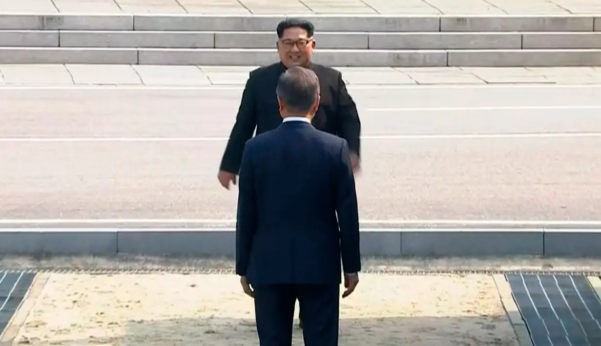 Presiden Korea Selatan, Moon Jae-in menyambut kedatangan Pemimpin Korea Utara, Kim Jong-un di Zona Demiliterisasi (DMZ), Panmunjom, Jumat (27/4). Keduanya berjabat tangan sambil menempatkan senyum di bibir masing-masing. (Korea Broadcasting System via AP)