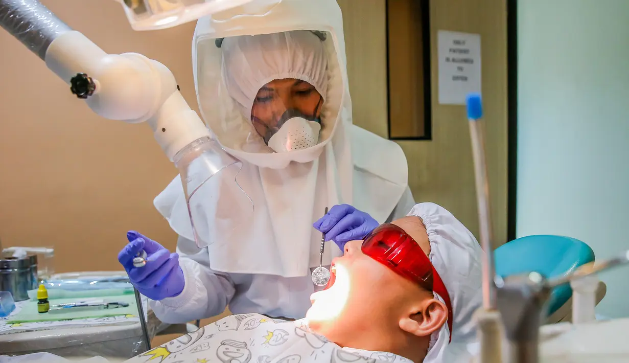 Dr. Maureen P. Ines-Manzano, seorang dokter gigi, memeriksa pasiennya di dalam kliniknya di Manila, Filipina, pada 19 Oktober 2020. Pasien Dr. Manzano menjulukinya "dokter gigi astronaut" karena mengenakan setelan PAPR untuk melindungi pasien dan dirinya dari COVID-19. (Xinhua/Rouelle Umali)