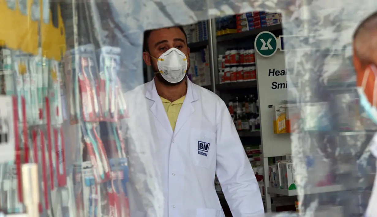 Pegawai melayani pembeli dari balik lapisan plastik untuk mengurangi kontak fisik di sebuah apotek di Baghdad, Irak, Selasa (14/4/2020). Kedispilinan masyarakat dalam menjaga jarak fisik atau physical distancing sangat berpengaruh dalam langkah meredam penyebaran virus corona COVID-19. (Xinhua)