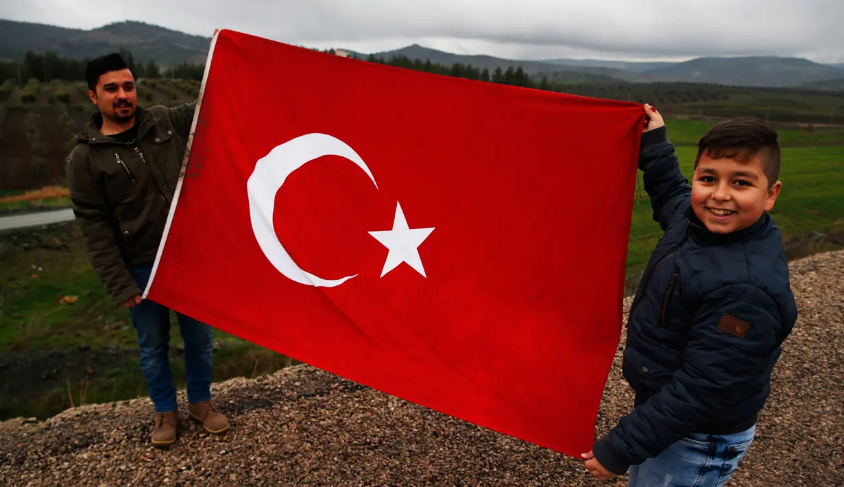 Dua pemuda membentangkan bendera sebagai dukungannya terhadap tentara Turki yang sedang memerangi milisi Kurdi di Suriah, Kilis, Turki, Jumat (26/1). (AP Photo/Lefteris Pitarakis)