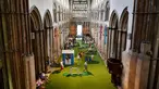Orang-orang bermain di lapangan golf kecil yang didirikan  di dalam Katedral Rochester, Inggris pada 6 Agustus 2019. Lapangan golf ini membentang di sepanjang lorong dan memiliki sembilan lubang dengan miniatur jembatan.  (Ben STANSALL / AFP)