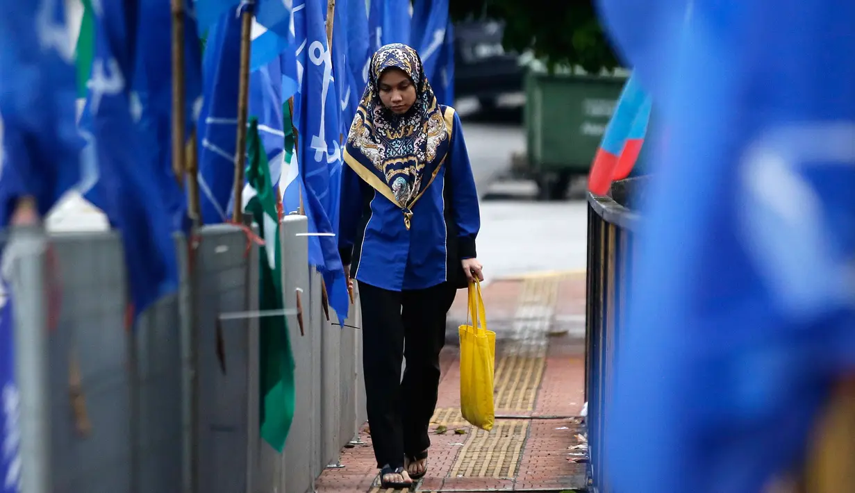 Seorang wanita berjalan di antara bendera partai politik, Kuala Lumpur, Malaysia, Senin (7/5). PM Malaysia Najib Razak akan bersaing dengan mantan mentornya, Mahathir Mohamad. (AP Photo/Aaron Favila)