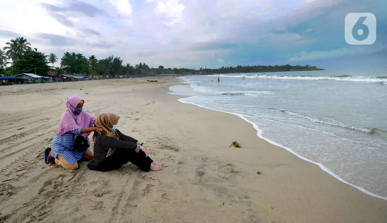 Wisatawan yang mengenakan masker menikmati suasana Pantai Anyer di Cilegon, Banten, Minggu (25/10/2020). Akhir pekan dimanfaatkan warga Jakarta dan sekitarnya untuk berwisata dengan tetap menerapkan protokol kesehatan Covid-19. (merdeka.com/Arie Basuki)