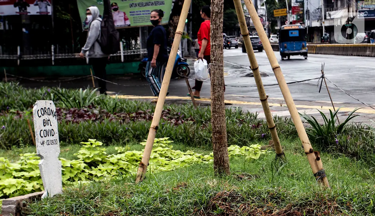 Warga melihat kuburan dengan papan nisan bertuliskan Corona bin Covid di taman Jalan Jatinegara Barat, Jakarta, Minggu (20/9/2020). Kuburan tersebut sengaja dibuat untuk mengingatkan masyarakat yang melintas akan bahaya virus Covid-19. (Liputan6.comm/Johan Tallo)