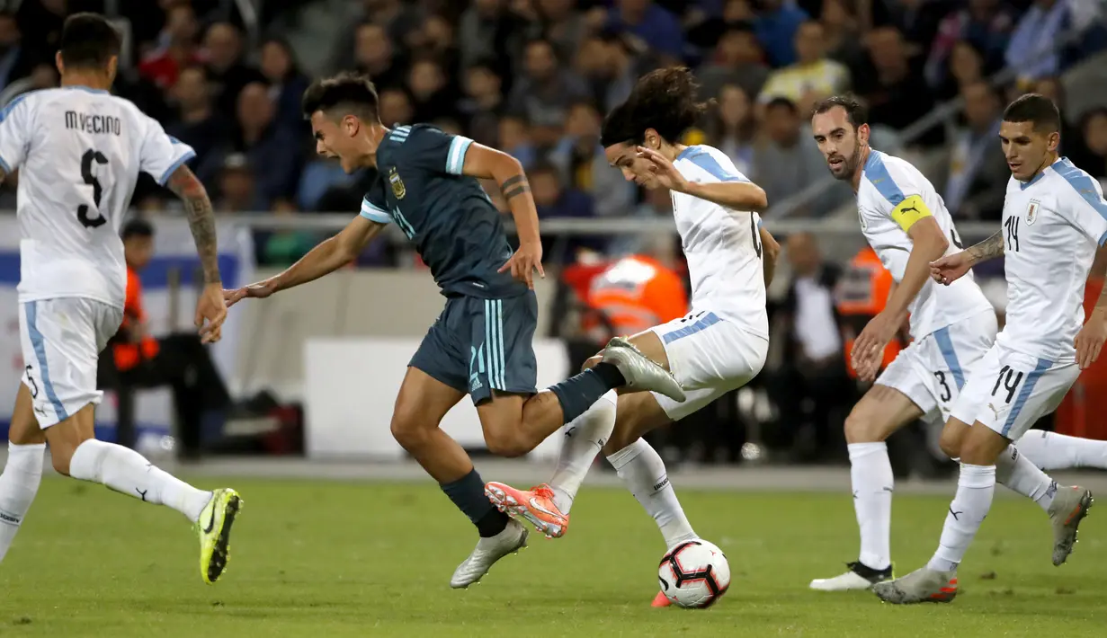 Pemain timnas Uruguay Edinson Cavani berebut bola dengan penyerang timnas Argentina Paulo Dybala dalam laga persahabatan di Stadion Bloomfield, Tel Aviv, Israel, Senin (18/11/2019). Skor berakhir 2-2, dengan penalti Lionel Messi menghindarkan timnas Argentina  dari kekalahan. (Jack GUEZ/AFP)