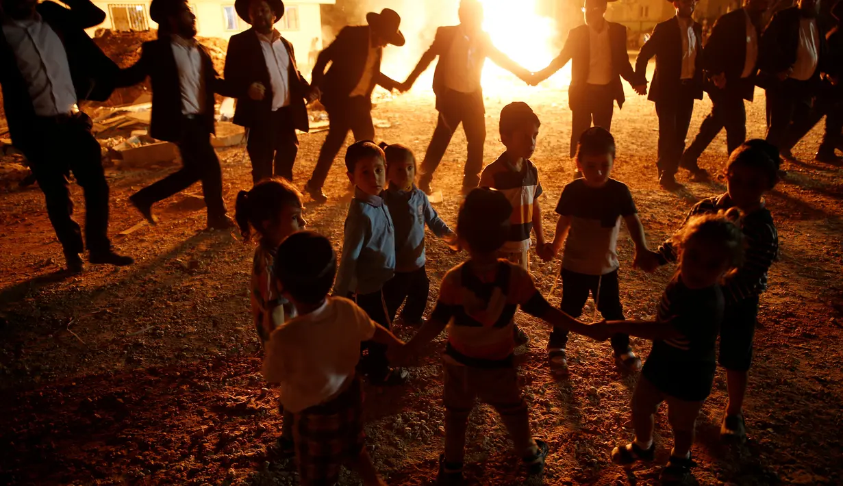 Anak-anak menari di samping api unggun selama perayaan hari libur Yahudi Lag Ba-Omer di Shearim, Yerusalem, (25/5). Lag Ba-Omer merupakan hari libur Yahudi yang dirayakan pada hari ke-33 dari Penghitungan Omer. (REUTERS/Ronen Zvulun)