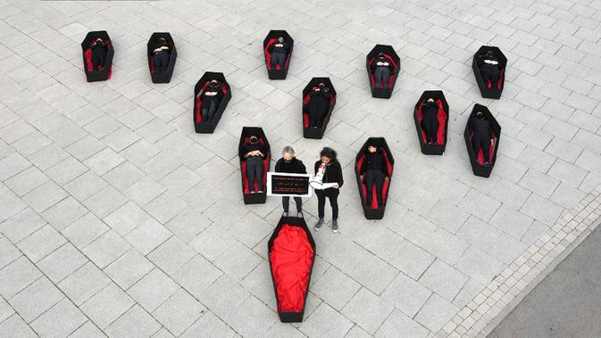 Para wanita berbaring dalam peti mati tiruan untuk mewakili mereka yang tewas akibat kekerasan dalam rumah tangga jelang Hari Perempuan Internasional di luar Pengadilan Distrik, Tel Aviv, Israel, Minggu (7/3/2021). Hari Perempuan Internasional dirayakan setiap tanggal 8 Maret. (JACK GUEZ/AFP)