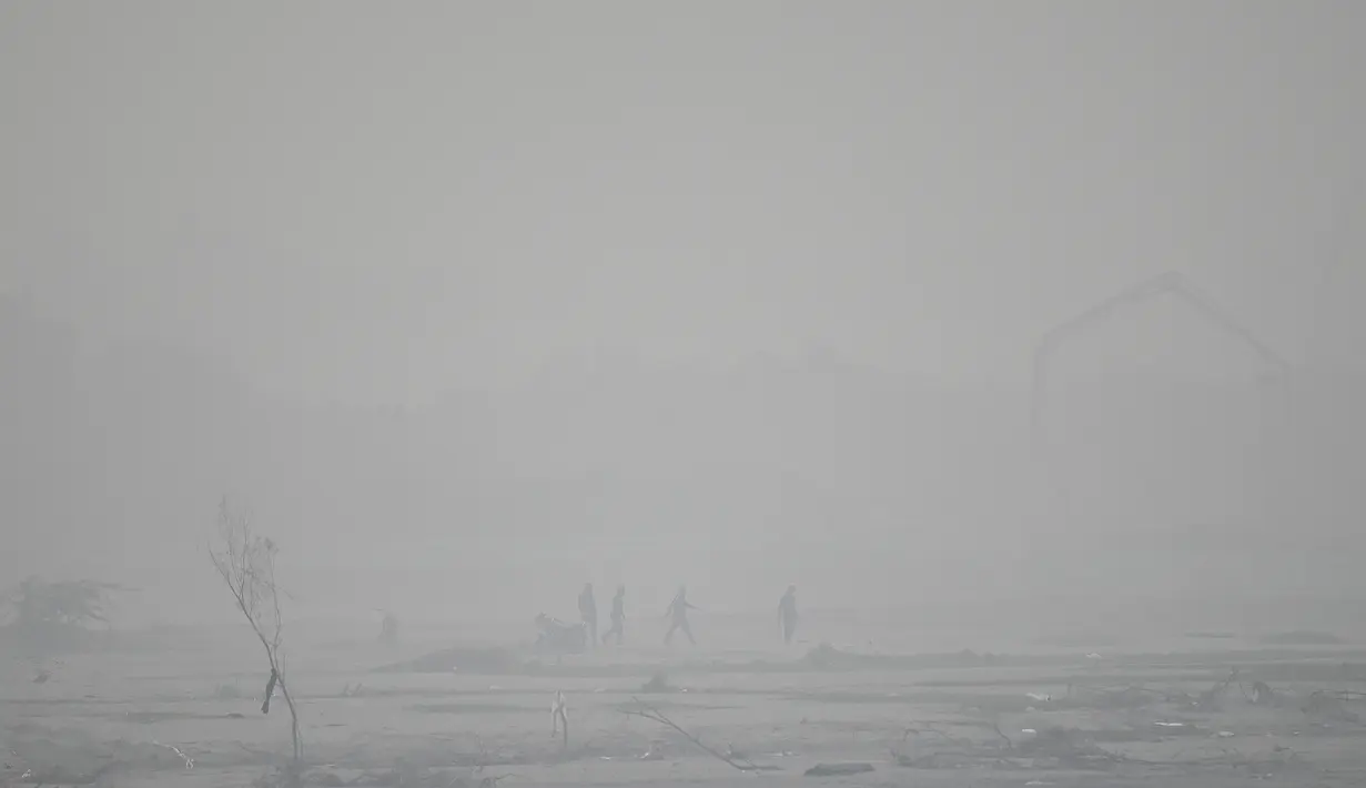 Orang-orang berjalan di sepanjang tepi sungai Yamuna di tengah kabut asap yang menyelimuti New Delhi, India, Minggu (7/11/2021). Ibu kota New Delhi diselimuti udara beracun pada Sabtu kemarin karena tingkat polusi yang sangat tinggi pasca-perayaan festival besar agama Hindu. (Money SHARMA/AFP)