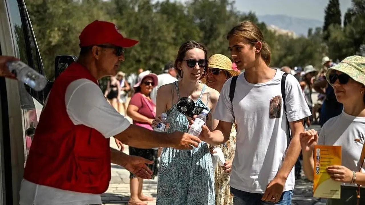 Suhu Yunani memanas. Seorang anggota organisasi Palang Merah Hellenic membagikan air dingin kepada wisatawan di dekat pintu masuk situs arkeologi Acropolis di Athena pada 20 Juli 2023. (AFP)