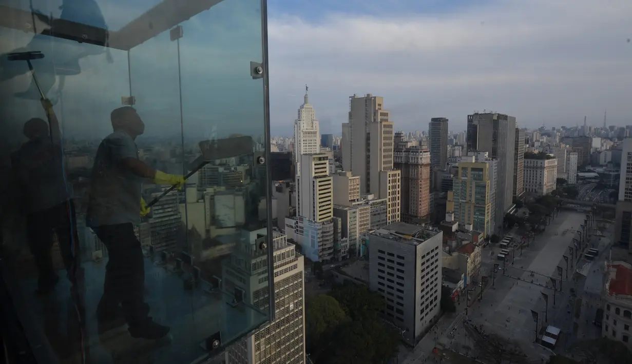Para pekerja membersihkan kaca jendela utama di Sampa Sky Observation Deck, di Sao Paulo, Brasil pada 05 Agustus 2021. Pengunjung mengalahkan rasa takut ketinggian untuk memandangi panorama sekaligus berpose di Sampa Sky. (NELSON ALMEIDA / AFP)