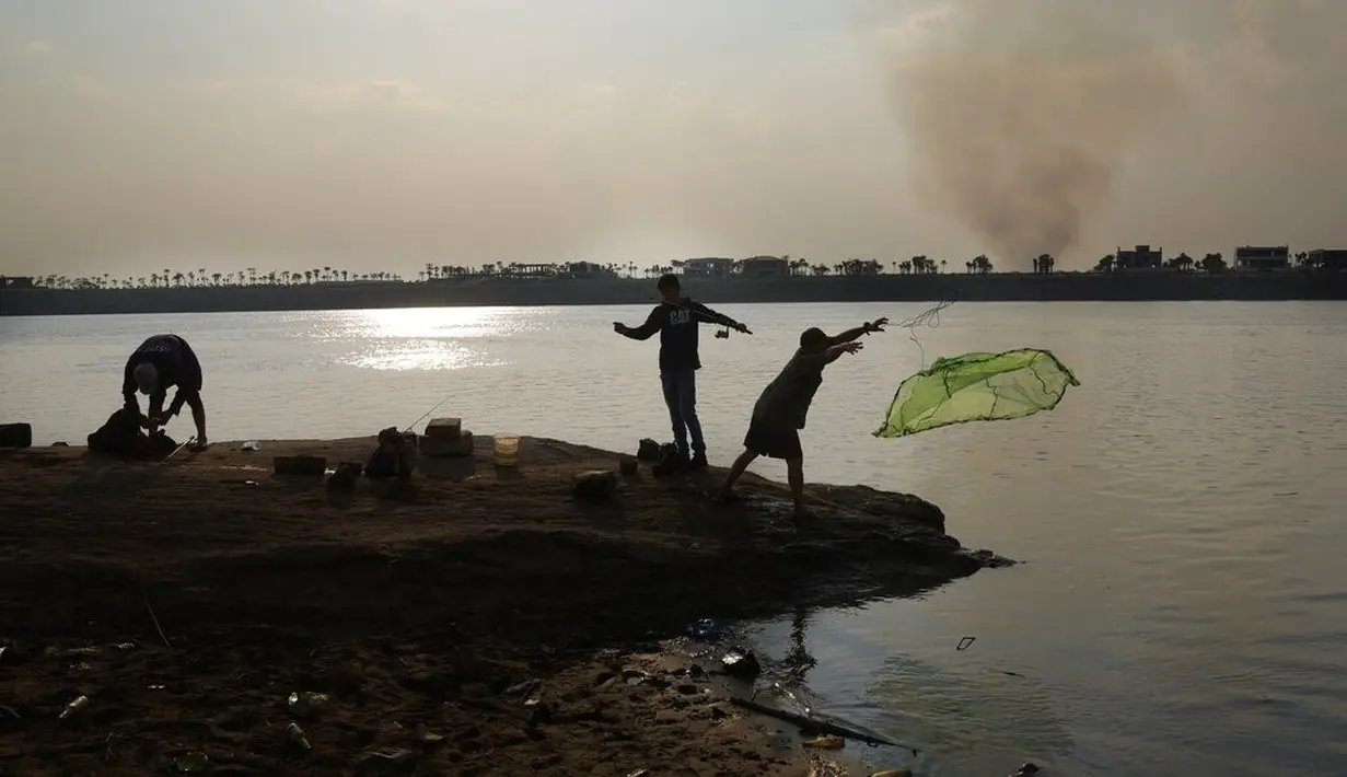 Orang-orang memancing di dasar sungai Paraguay yang terbuka, saat kolom asap membubung di pantai lain, di tengah kekeringan bersejarah yang mempengaruhi ketinggian sungai, di Mariano Roque Alonso, Paraguay, Senin (20/9/2021).  (AP Photo/Jorge Saenz)